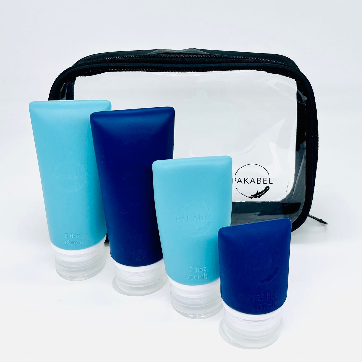 Set of 4 refillable travel bottles in three sizes and two colours. Navy blue and teal sitting in front of a clear toiletry bag