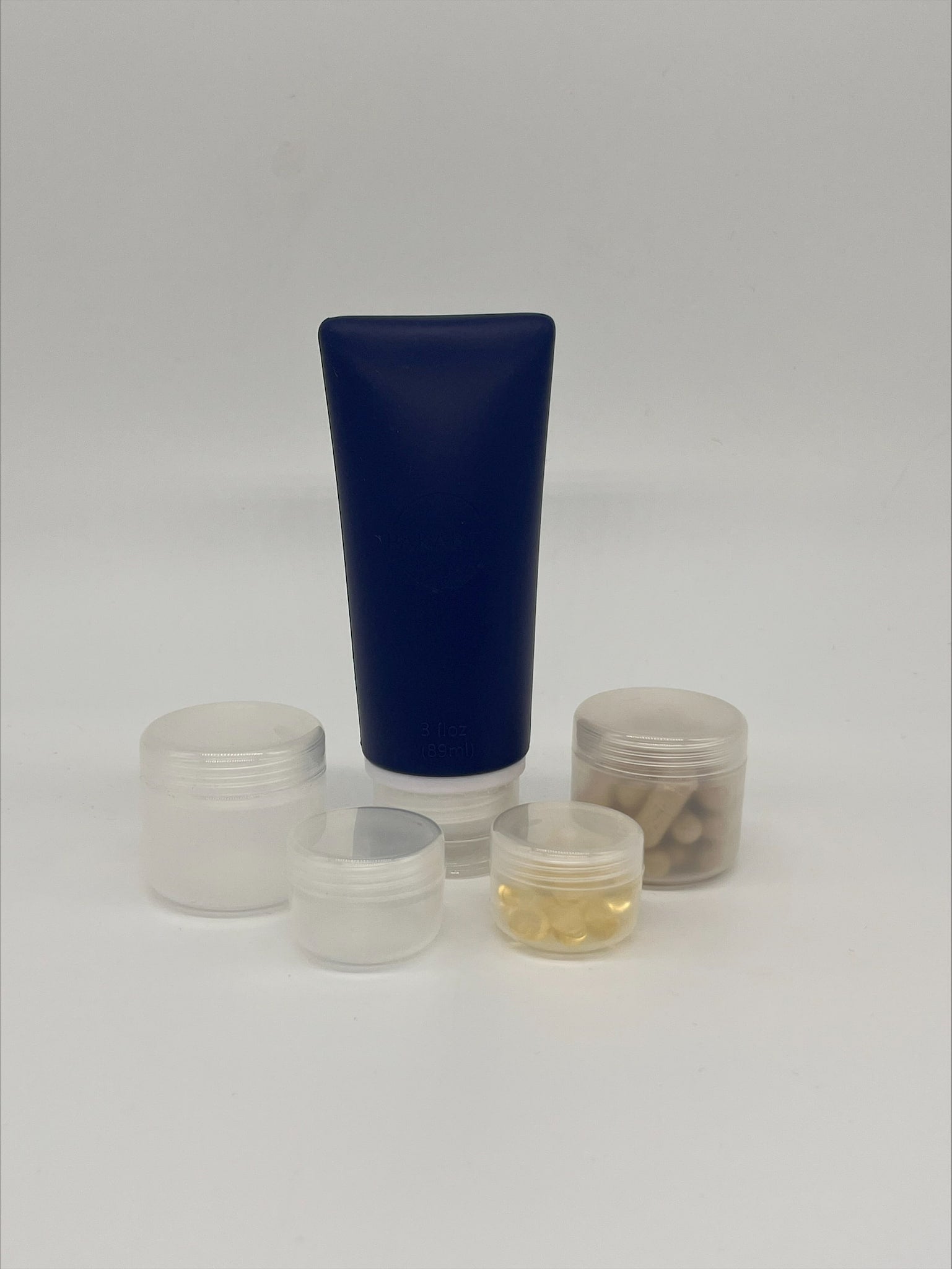 navy blue refillable toiletry bottle surrounded by 4 frosted plastic refillable pots containing vitamin tablets